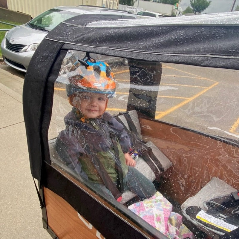 Toddler in bunch bike on rainy day with rain tent #color_Honey Woodgrain