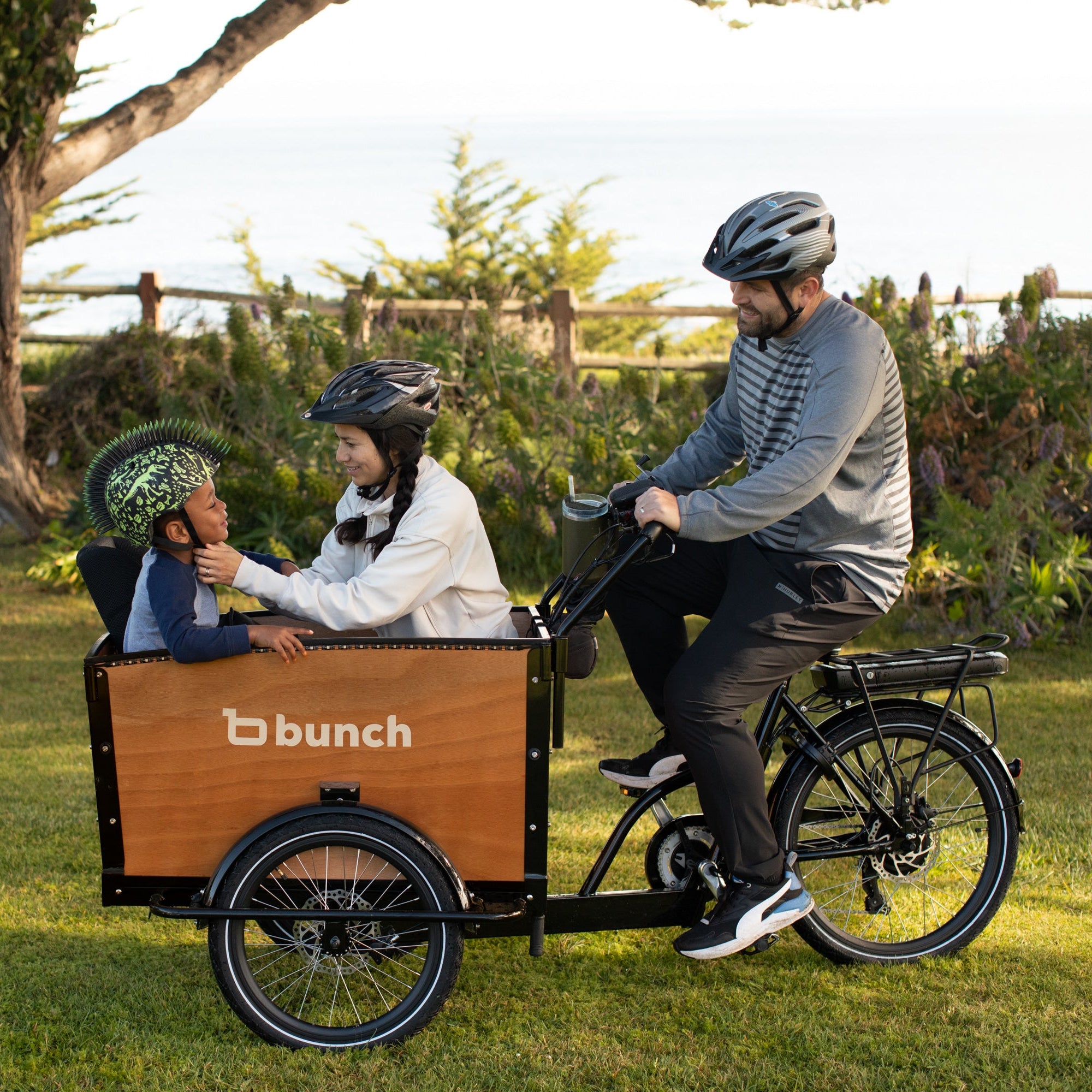 Family using a 'bunch' brand cargo bike in a park setting #color_Honey Woodgrain